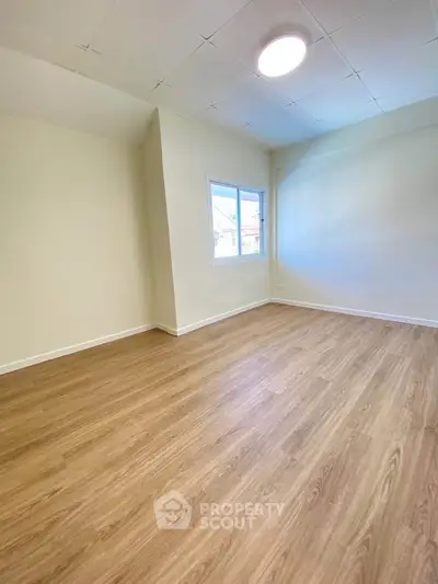 Spacious empty room with wooden flooring and natural light from window.