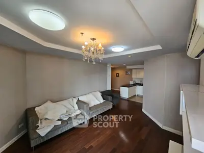 Spacious living room with elegant chandelier and cozy seating area in modern apartment.