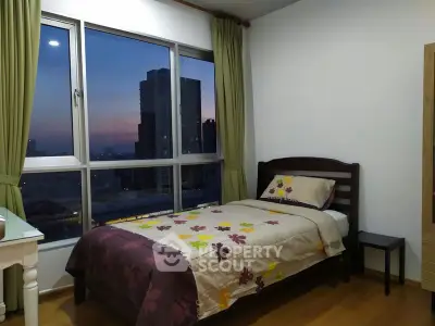 Cozy bedroom with city view, featuring a single bed and large window with curtains.
