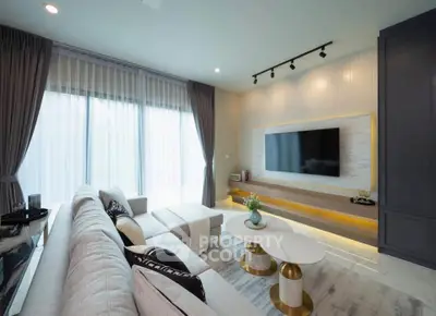 Modern living room with stylish decor and large TV, featuring elegant furniture and natural light.