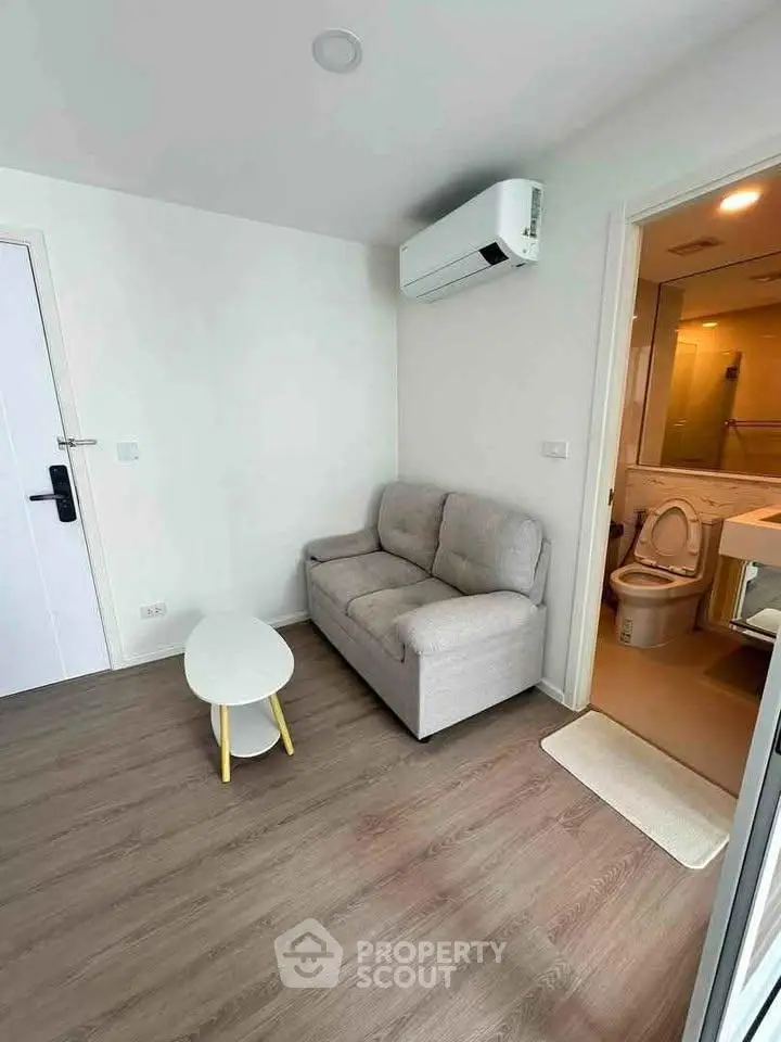 Cozy living room with modern sofa and air conditioning, adjacent to a compact bathroom.