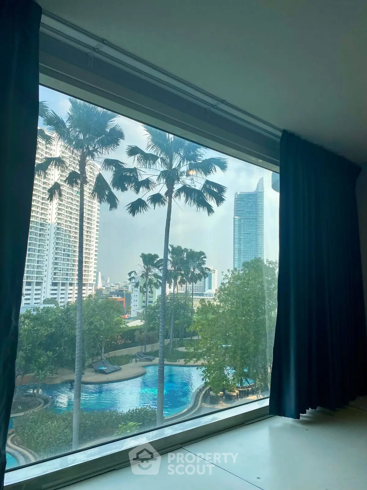 Stunning high-rise view with pool and palm trees from large window.