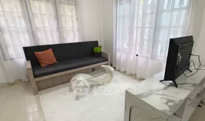 Bright living room with modern sofa and TV, featuring large windows and elegant decor.