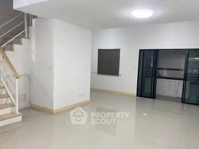 Spacious modern living room with staircase and glass doors leading to kitchen.