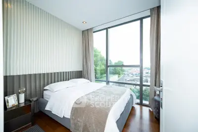 Modern bedroom with large window and city view, featuring stylish decor and cozy bedding.