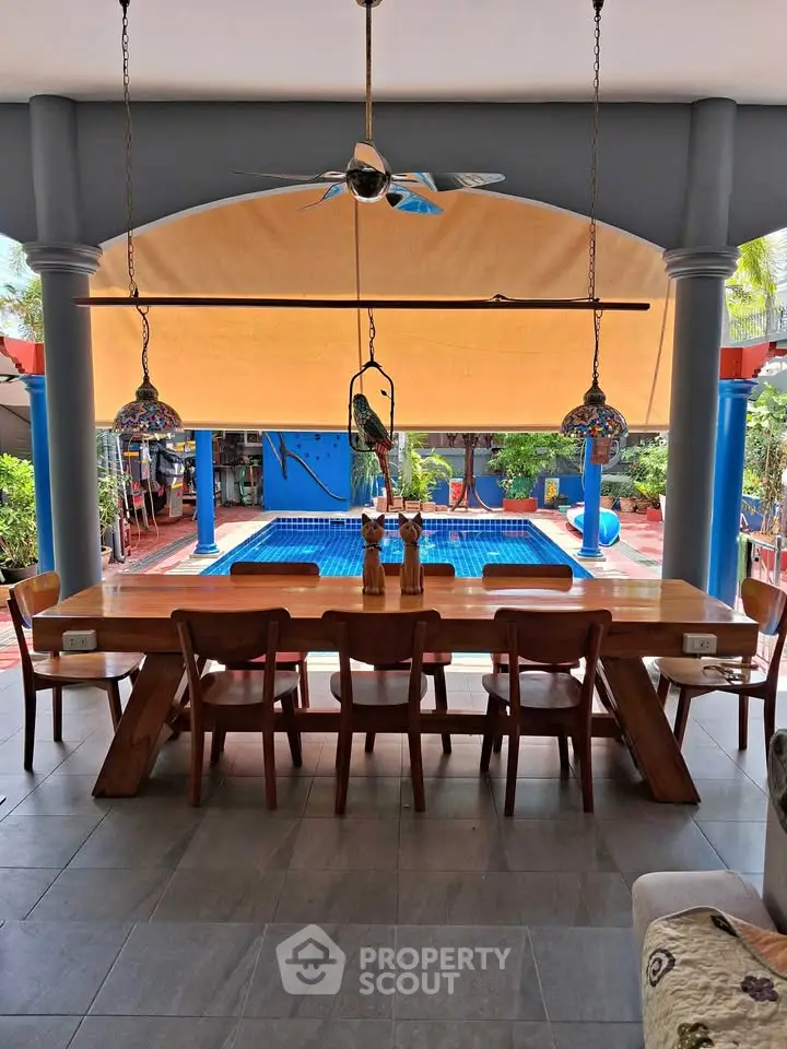 Luxurious outdoor dining area with pool view, featuring elegant wooden furniture and vibrant decor.