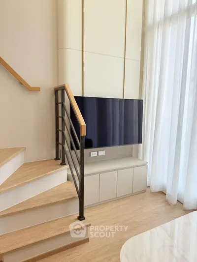 Modern living room with sleek staircase and mounted TV, featuring floor-to-ceiling windows.