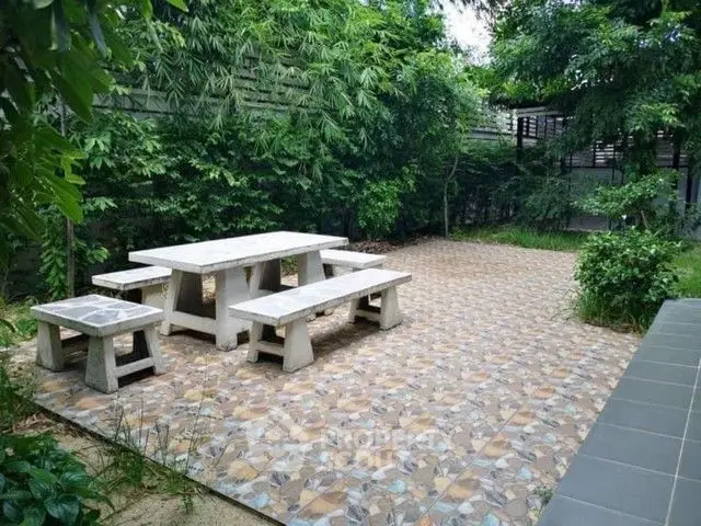 Charming garden patio with stone benches and lush greenery, perfect for outdoor relaxation.