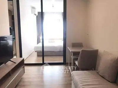 Modern apartment interior with cozy living area and bedroom separated by glass partition.