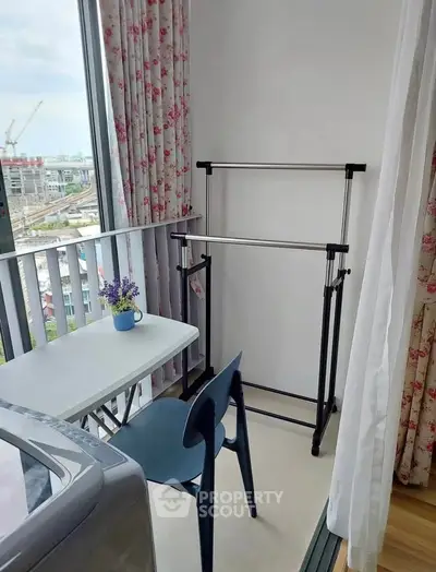 Charming balcony with city view, featuring a cozy table, chair, and floral curtains, perfect for relaxation.