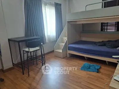 Modern bedroom with loft bed and study area, featuring wooden flooring and natural light.