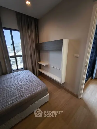 Modern bedroom with wooden flooring and large window offering city views.