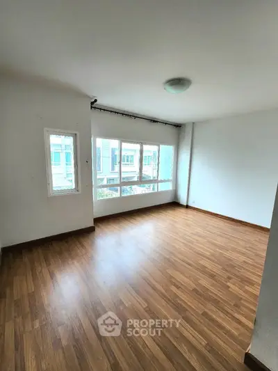 Spacious empty room with wooden flooring and large windows for natural light.