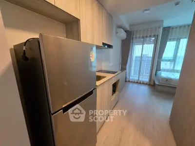 Modern studio apartment with sleek kitchen and cozy bedroom area, featuring a stainless steel fridge and large windows.