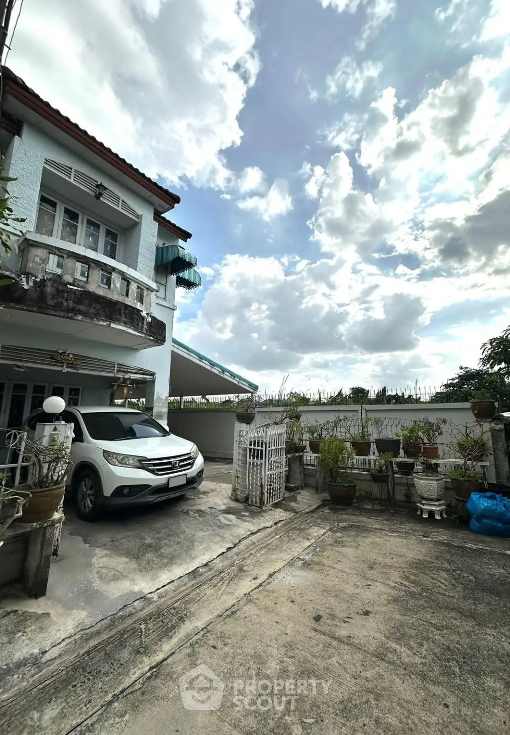 Charming suburban home with spacious driveway and lush potted plants under a picturesque sky.