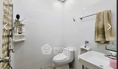 Modern bathroom with white tiles, toilet, urinal, and sink, featuring a towel rack and shower area.