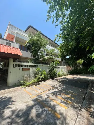 Charming residential building with lush greenery and spacious driveway under clear blue sky.