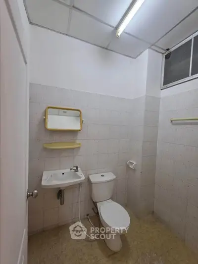 Simple bathroom with white tiles, toilet, sink, and mirror in a real estate property.