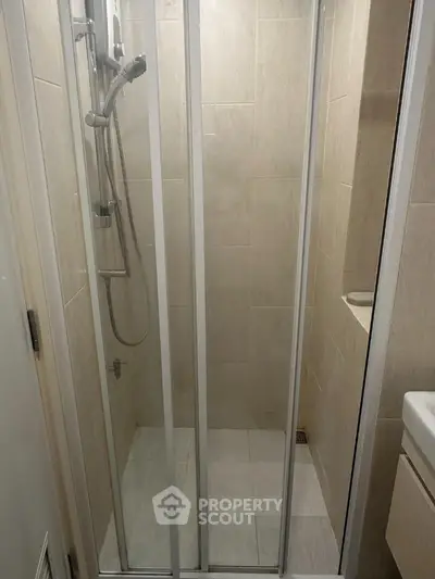 Compact bathroom shower area with modern sliding glass doors and beige tiles.