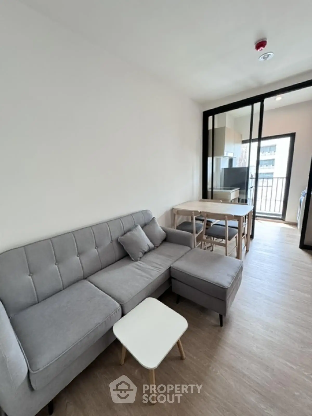 Modern living room with gray sofa and open layout leading to kitchen and balcony.