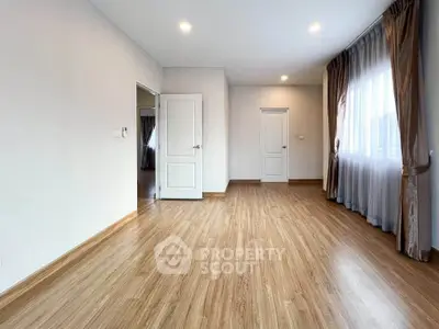 Spacious empty room with wooden flooring and natural light, perfect for customization.