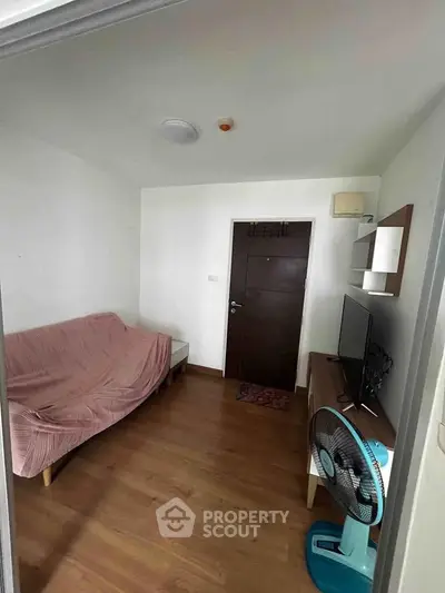 Cozy living room with wooden flooring, sofa, TV, and fan, perfect for relaxation.