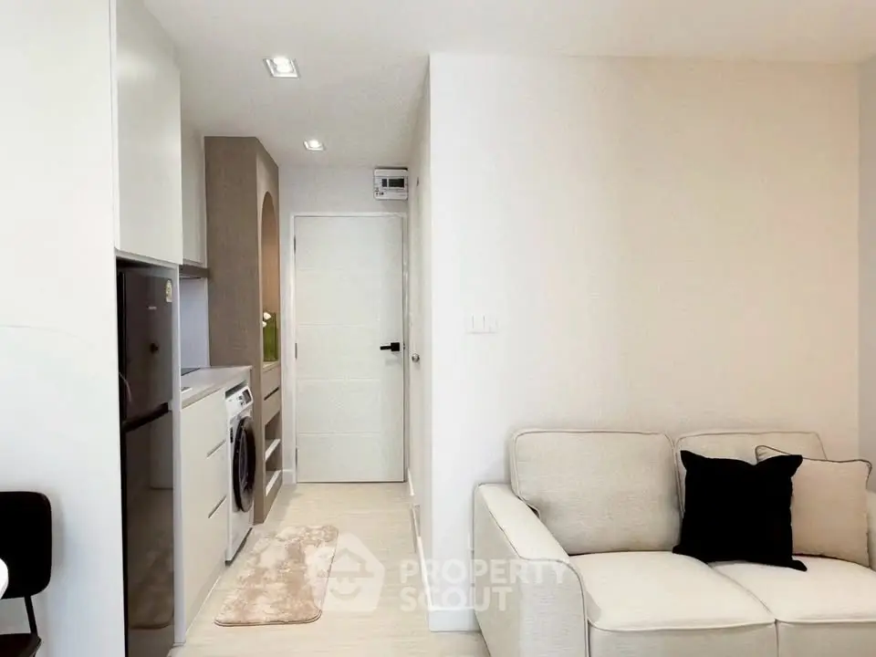 Modern apartment interior with cozy living room and compact kitchen featuring washing machine and fridge.