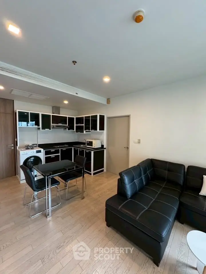 Modern open-layout kitchen and living room with sleek black furniture and wooden flooring.