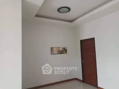 Minimalist interior with white walls and wooden door, featuring a ceiling light and wall art.