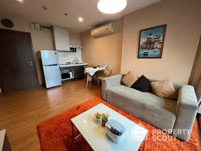 Spacious studio apartment with integrated living area and kitchen, featuring modern appliances, plush sofa, and vibrant red rug, perfect for urban living.