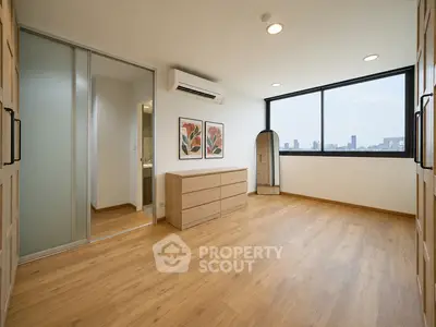 Spacious bedroom with wooden flooring and city view, featuring modern decor and ample natural light.
