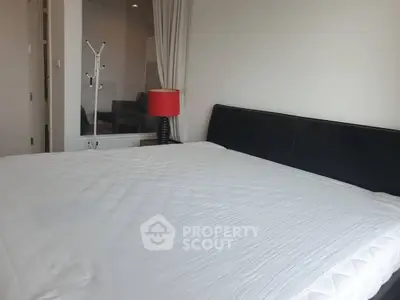 Spacious bedroom with modern decor and large bed, featuring a stylish red lamp and sleek black headboard.