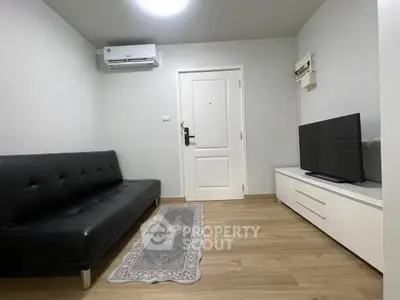 Modern living room with sleek black sofa and flat-screen TV, featuring minimalist decor and wooden flooring.