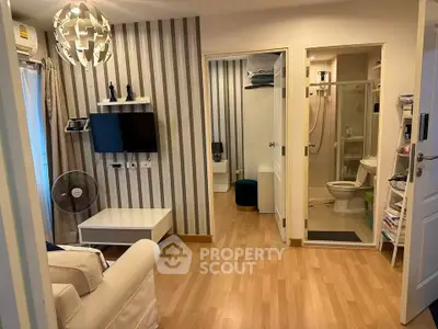 Modern living room with stylish decor and adjacent bathroom, featuring wooden flooring and contemporary lighting.