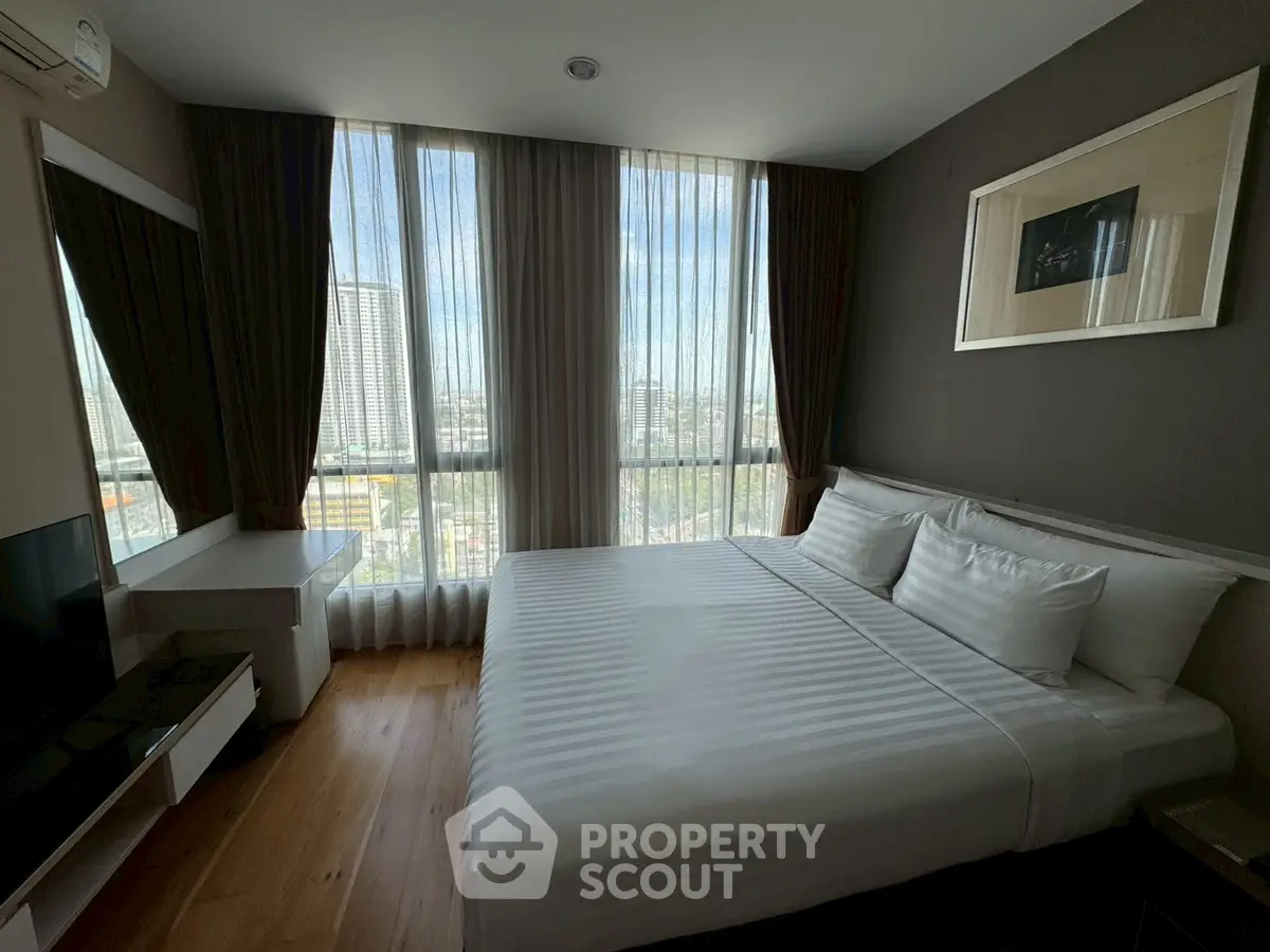 Modern bedroom with large windows and city view, featuring a comfortable bed and sleek decor.