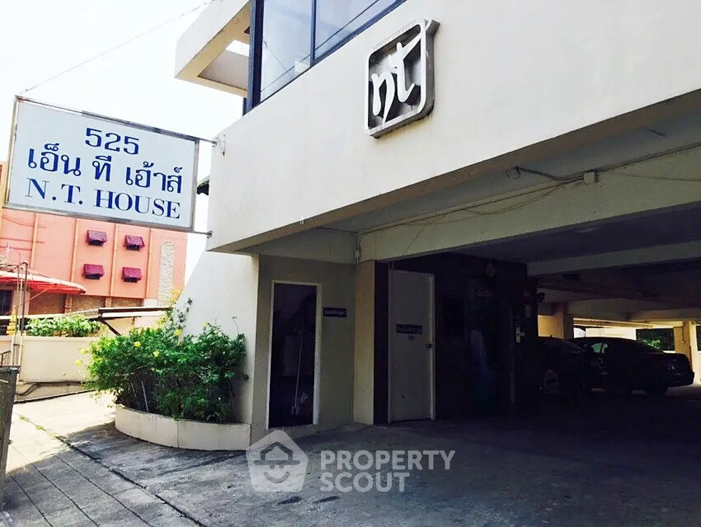 Modern entrance of N.T. House with parking area and lush greenery, ideal for urban living.