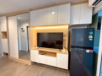Modern living room with sleek cabinetry and large TV, featuring a stylish fridge and ambient lighting.