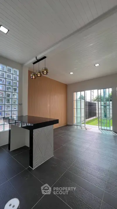 Modern open-plan living area with stylish lighting and large glass doors leading to a lush garden.