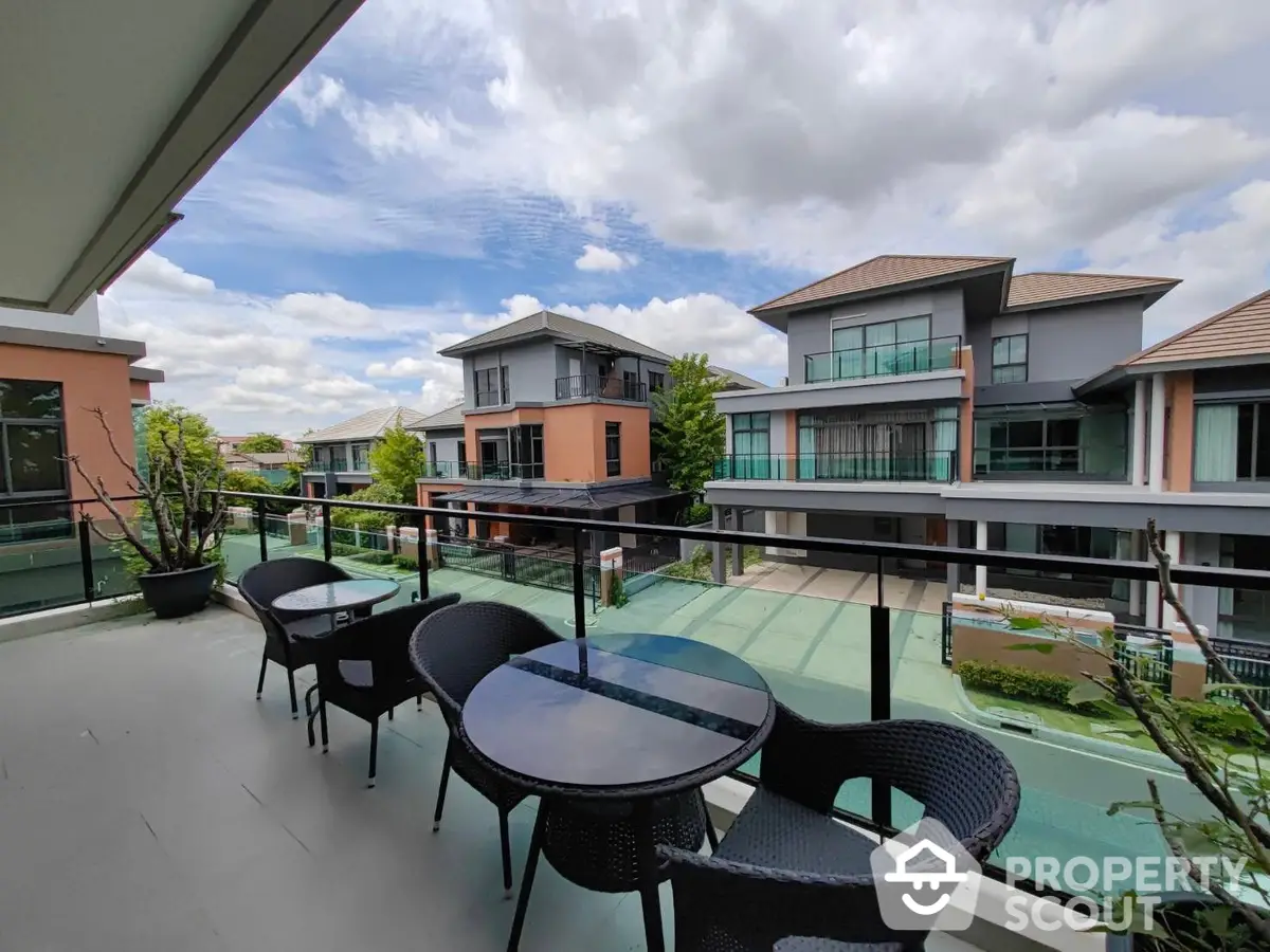 Spacious balcony with outdoor seating overlooking a serene pool and modern suburban homes, perfect for relaxing and entertaining.