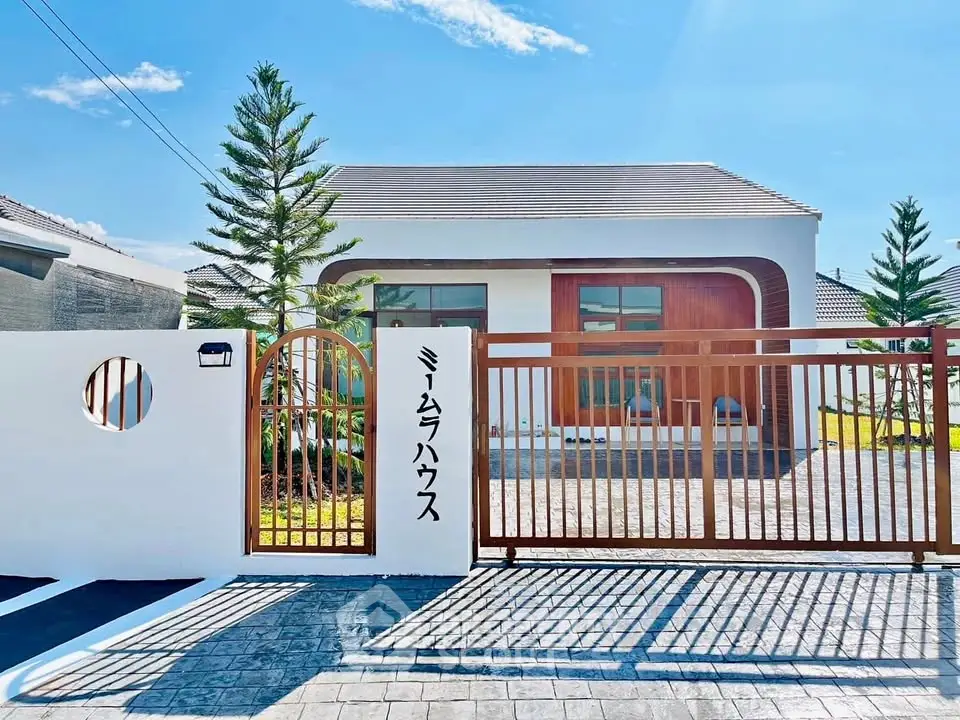 Modern single-story house with stylish gate and lush landscaping under a clear blue sky.