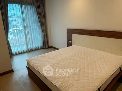Spacious bedroom with large window and modern furnishings in a stylish apartment.
