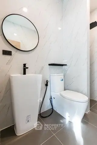 Modern bathroom with sleek fixtures and minimalist design, featuring a round mirror and elegant sink.