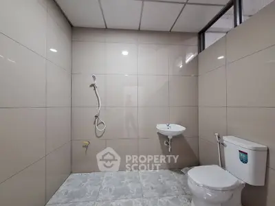 Modern bathroom with sleek tiles and minimalist fixtures, featuring a shower, sink, and toilet.