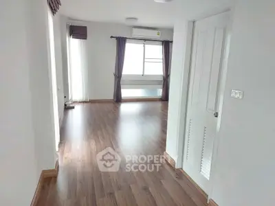 Spacious empty room with wooden flooring and large windows, perfect for customization.