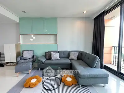 Modern living room with stylish gray sectional sofa and glass coffee table, featuring large windows and chic decor.