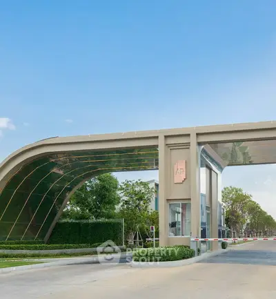 Elegant gated entrance of a modern residential community with lush greenery and clear blue skies.