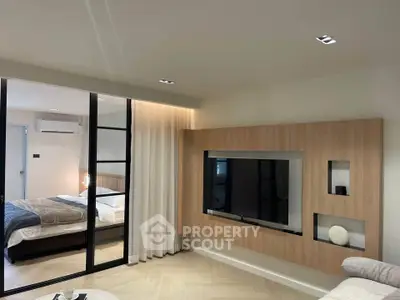 Modern living room with sleek TV wall unit and view into cozy bedroom