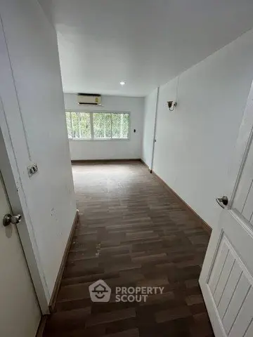 Spacious empty room with wooden flooring and large window offering natural light.