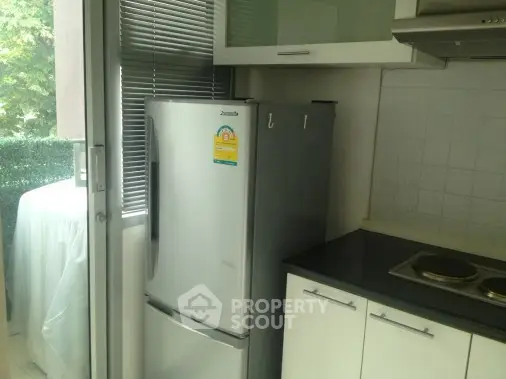 Modern kitchen with sleek fridge and electric stove, adjacent to a bright balcony view.