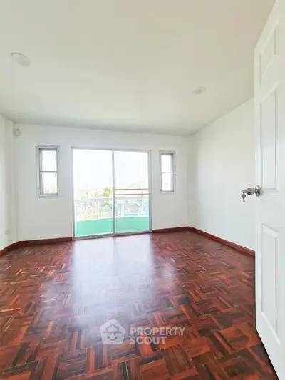 Spacious empty room with wooden flooring and balcony access